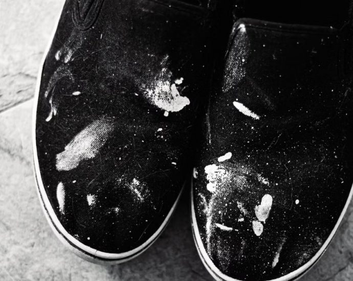 Close-up of black sneakers with white paint splashes on tile floor, showcasing texture and contrast.