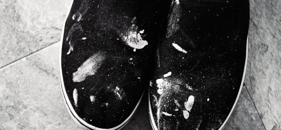Close-up of black sneakers with white paint splashes on tile floor, showcasing texture and contrast.