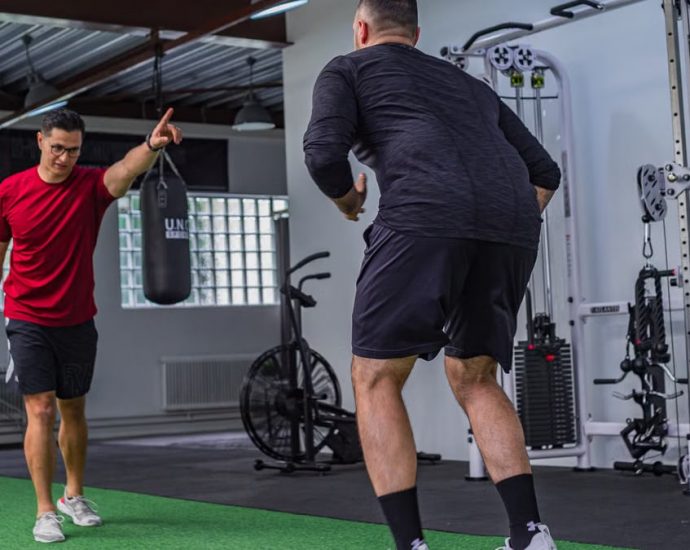 Back view of muscular man in sportswear doing exercises with trainer in modern fitness club
